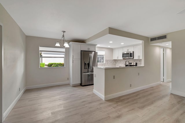 kitchen featuring white cabinets, kitchen peninsula, light hardwood / wood-style flooring, backsplash, and stainless steel appliances