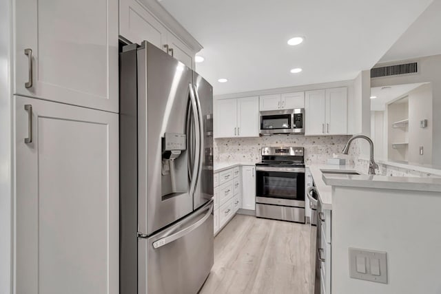 kitchen with white cabinets, appliances with stainless steel finishes, light wood-type flooring, and sink