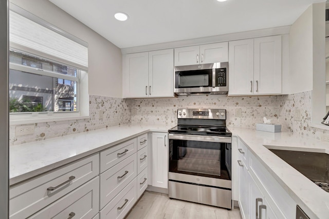 kitchen with sink, white cabinetry, light hardwood / wood-style flooring, stainless steel appliances, and light stone countertops