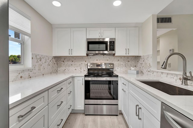 kitchen with white cabinets, ceiling fan with notable chandelier, stainless steel appliances, light wood-type flooring, and sink