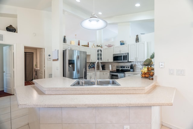 kitchen featuring kitchen peninsula, appliances with stainless steel finishes, light tile flooring, white cabinets, and sink