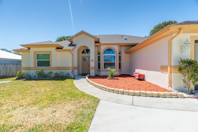 view of front of house featuring stucco siding, a shingled roof, a front lawn, and fence