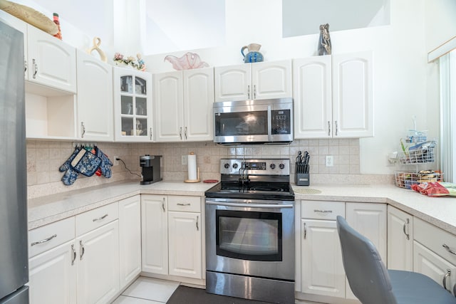 kitchen with appliances with stainless steel finishes, light tile floors, backsplash, and white cabinets