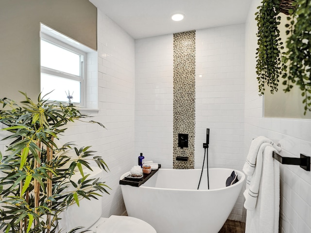 bathroom with a tub to relax in and tile walls