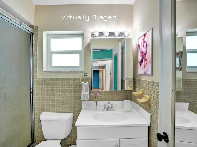 bathroom with vanity, toilet, a shower with shower door, and tile walls