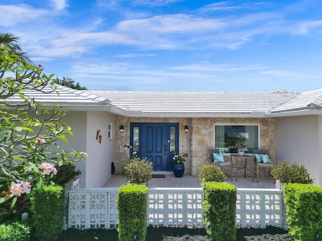 entrance to property with a porch, stone siding, a tile roof, and stucco siding