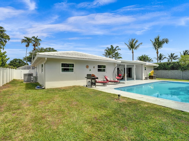 rear view of house with a lawn, cooling unit, a fenced in pool, and a patio