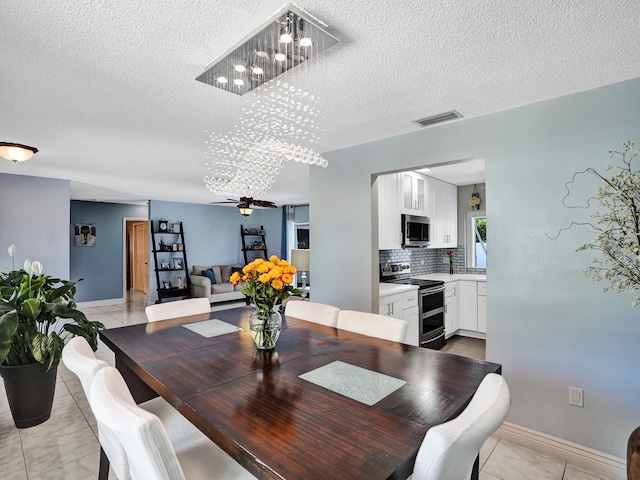 dining area featuring ceiling fan with notable chandelier, light tile patterned flooring, and a textured ceiling