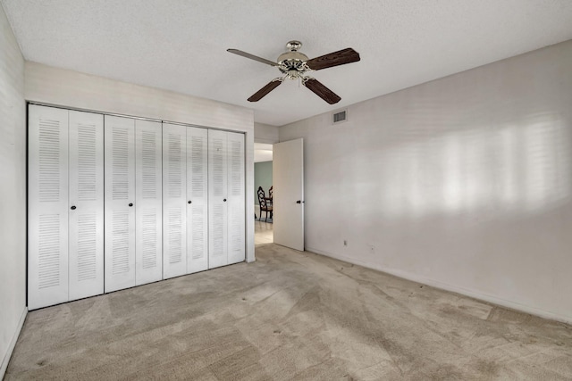 unfurnished bedroom featuring light colored carpet, ceiling fan, a textured ceiling, and a closet