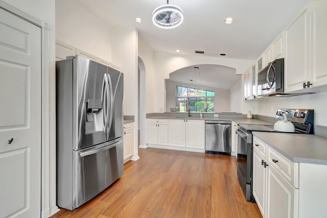 kitchen with lofted ceiling, white cabinets, hanging light fixtures, light hardwood / wood-style flooring, and stainless steel appliances