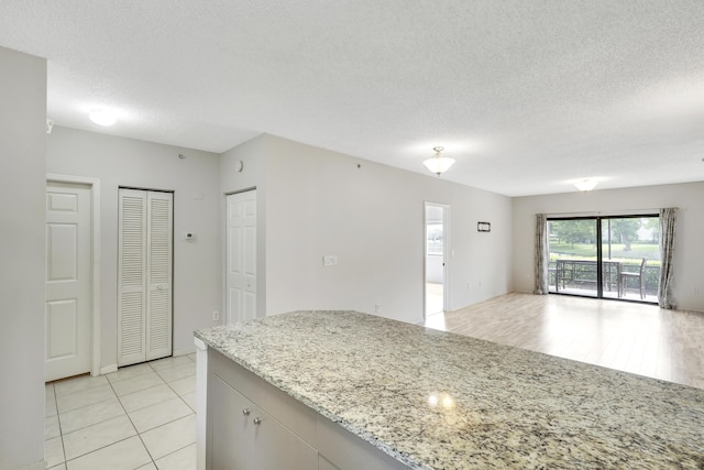 kitchen with white cabinets, light stone counters, light wood-type flooring, and a textured ceiling