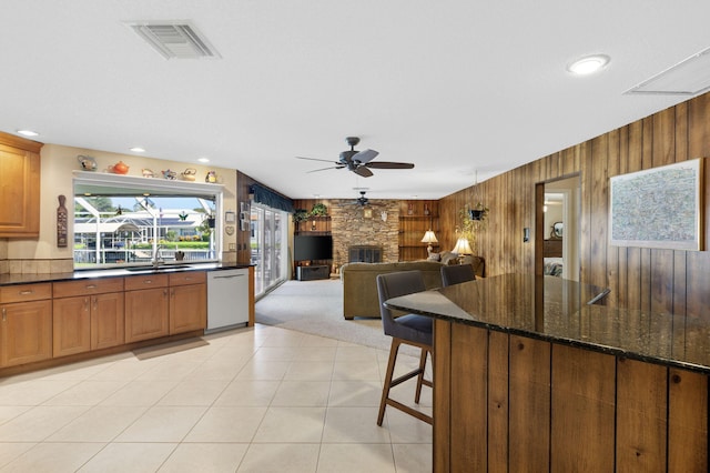 kitchen featuring a fireplace, sink, dishwasher, wood walls, and dark stone countertops