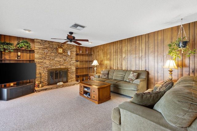 living room featuring wooden walls, light carpet, a stone fireplace, ceiling fan, and a textured ceiling