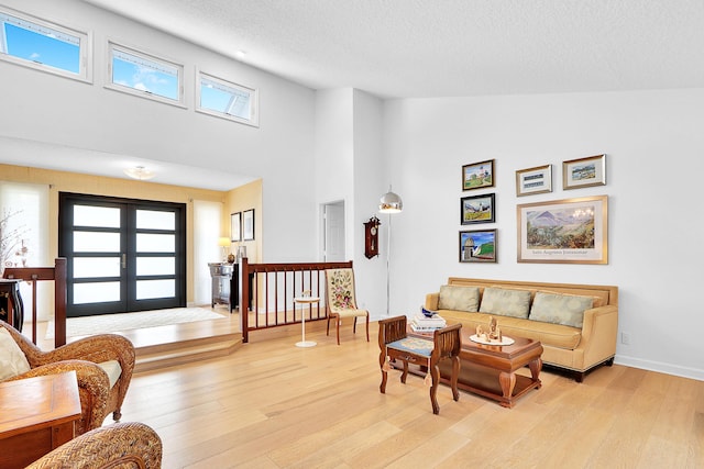 living room featuring a towering ceiling, french doors, light hardwood / wood-style floors, and a textured ceiling