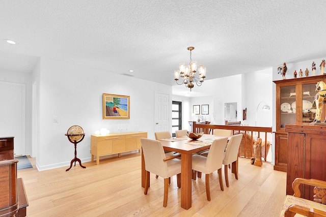 dining room with a textured ceiling, light hardwood / wood-style flooring, and an inviting chandelier