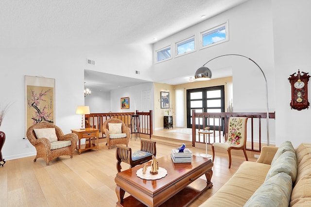 living room featuring light hardwood / wood-style flooring, a high ceiling, a wealth of natural light, and french doors