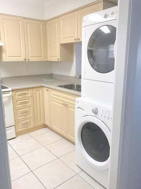 laundry room featuring cabinets, light tile floors, sink, and stacked washer / drying machine