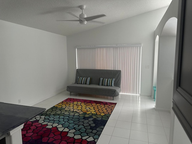 interior space featuring ceiling fan, a textured ceiling, vaulted ceiling, and light tile patterned floors