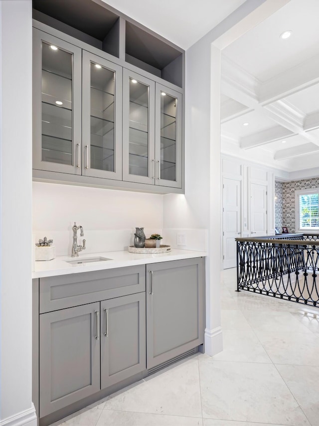 bar with beamed ceiling, sink, gray cabinetry, and coffered ceiling