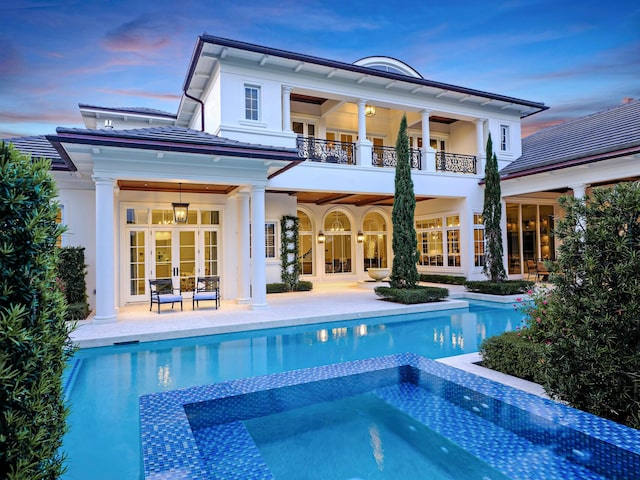 back house at dusk featuring a patio area, french doors, and a balcony