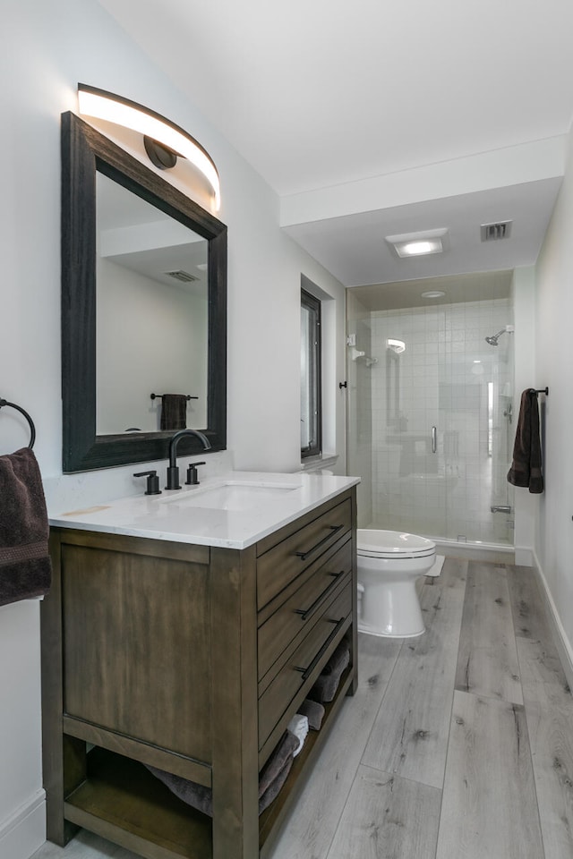 bathroom with wood-type flooring, vanity, toilet, and a shower with shower door