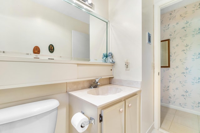 bathroom featuring toilet, vanity, tile patterned flooring, baseboards, and wallpapered walls