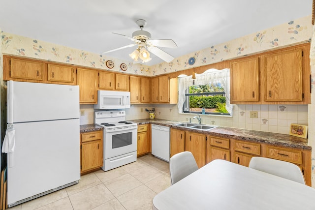 kitchen with white appliances, dark countertops, a sink, and wallpapered walls