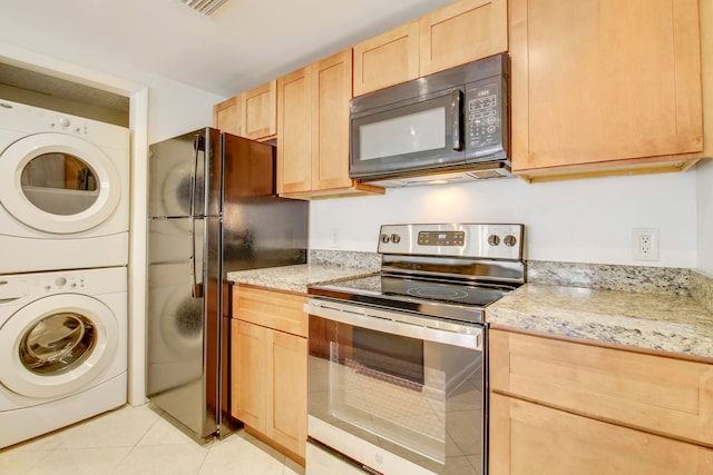 kitchen with light brown cabinetry, stacked washer and clothes dryer, light tile floors, and black appliances