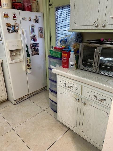 kitchen with light brown cabinetry, white refrigerator with ice dispenser, tile counters, and light tile floors