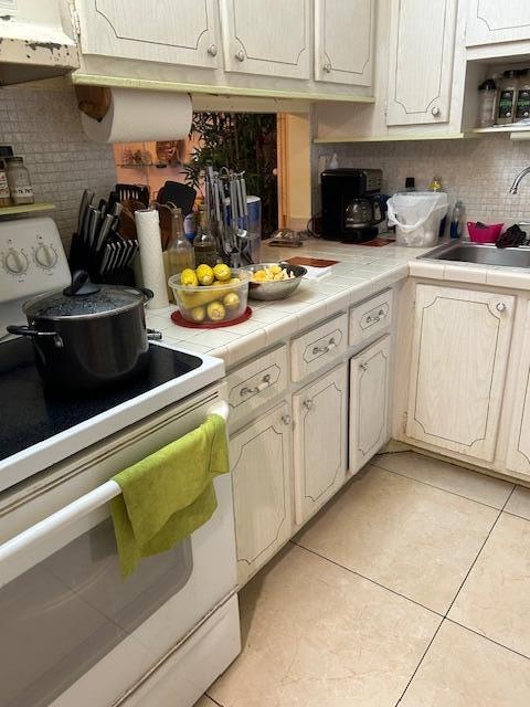 kitchen featuring backsplash, sink, light tile floors, white range with electric cooktop, and tile countertops