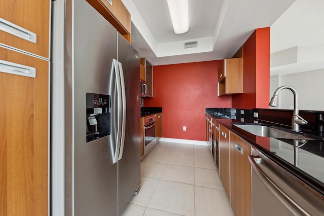 kitchen with sink, light tile patterned floors, stainless steel appliances, and a tray ceiling