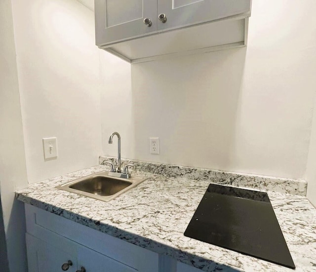 kitchen with sink, blue cabinetry, black electric cooktop, and light stone counters