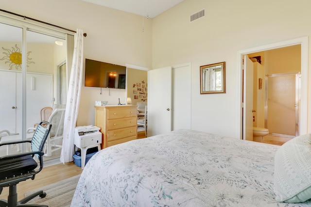 bedroom featuring a closet, light hardwood / wood-style flooring, ensuite bathroom, and a high ceiling