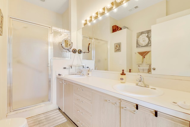 bathroom featuring a shower with shower door, toilet, and double sink vanity