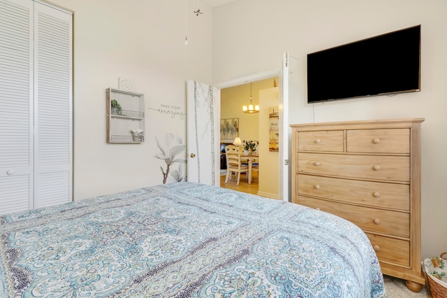 bedroom with light hardwood / wood-style flooring, a towering ceiling, and a notable chandelier