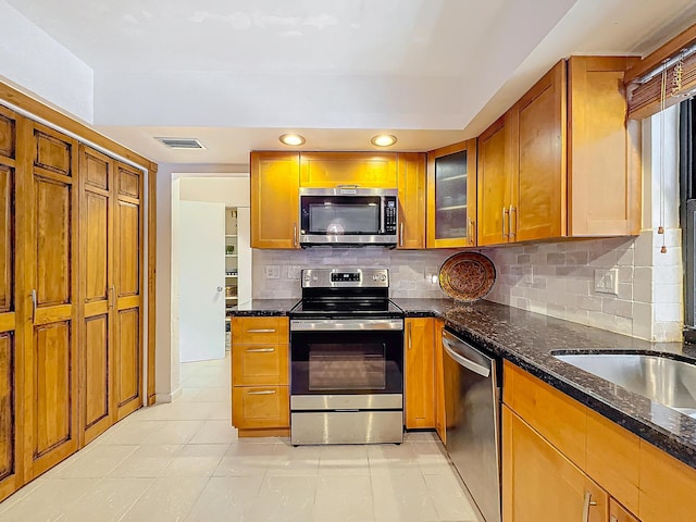 kitchen featuring light tile patterned flooring, appliances with stainless steel finishes, backsplash, and dark stone countertops