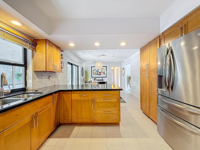 kitchen featuring pendant lighting, sink, stainless steel fridge, dark stone countertops, and kitchen peninsula