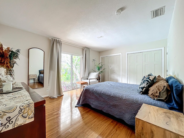 bedroom featuring a textured ceiling, access to exterior, light hardwood / wood-style flooring, and two closets