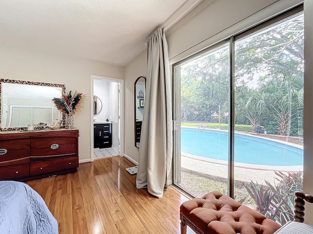 bedroom featuring access to outside, vaulted ceiling, ensuite bathroom, and light hardwood / wood-style flooring