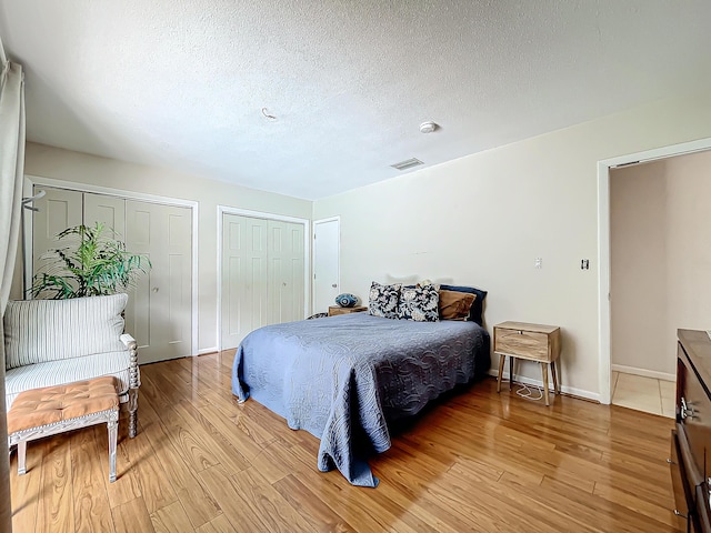 bedroom featuring a textured ceiling, light hardwood / wood-style flooring, and multiple closets