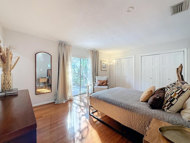 bedroom featuring hardwood / wood-style flooring, access to exterior, and two closets