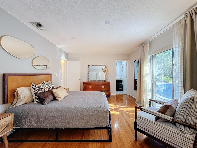 bedroom featuring a textured ceiling, connected bathroom, and light hardwood / wood-style flooring