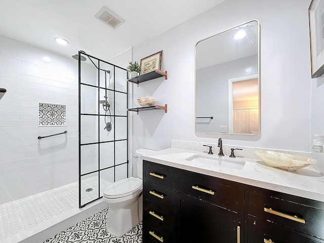 bathroom with tile patterned flooring, vanity, tiled shower, and toilet