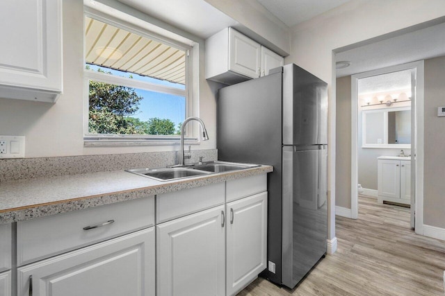 kitchen featuring sink, stainless steel fridge, light wood-type flooring, and white cabinetry