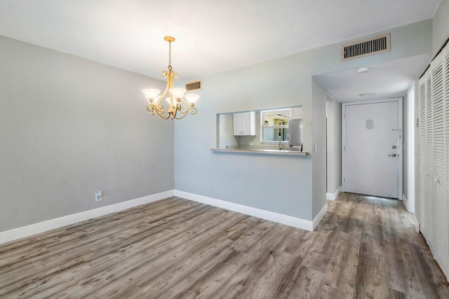 unfurnished room with a textured ceiling, hardwood / wood-style floors, and a notable chandelier