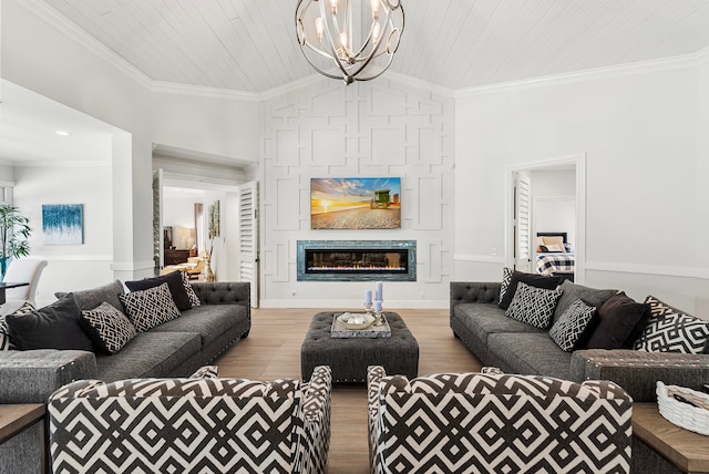 living room with a fireplace, light hardwood / wood-style flooring, ornamental molding, an inviting chandelier, and vaulted ceiling