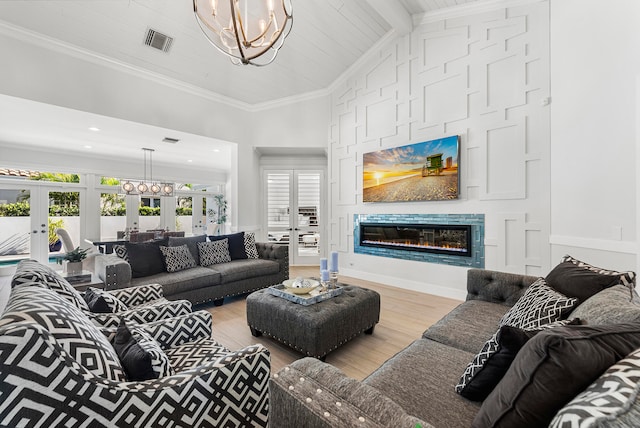 living room featuring french doors, lofted ceiling with beams, light wood-type flooring, a chandelier, and ornamental molding