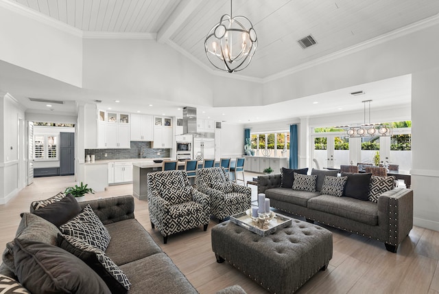 living room with beamed ceiling, light hardwood / wood-style flooring, a high ceiling, french doors, and an inviting chandelier