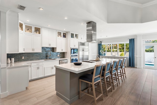 kitchen with built in appliances, tasteful backsplash, island exhaust hood, white cabinetry, and a center island