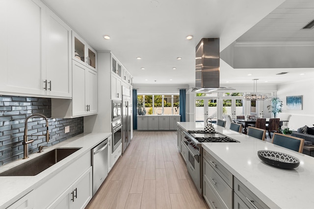 kitchen with backsplash, crown molding, island range hood, white cabinets, and sink